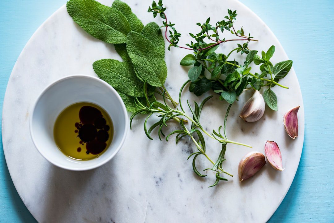 Una tavola di marmo con erbe fresche, spicchi d’aglio e una piccola ciotola bianca contenente olio d’oliva e aceto balsamico, disposti su una superficie azzurra. Una tavola di marmo con erbe fresche, spicchi d'aglio e una piccola ciotola bianca contenente olio d'oliva e aceto balsamico, disposti su una superficie azzurra.